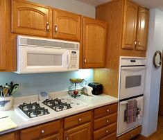 a kitchen with wooden cabinets and white appliances, including a microwave above the stove top