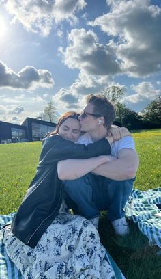 two people sitting on top of a blanket in the middle of a grass covered field