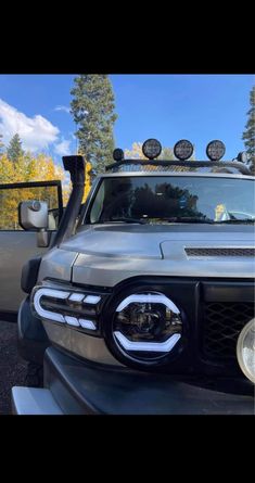 the front end of a silver truck parked in a parking lot with trees behind it