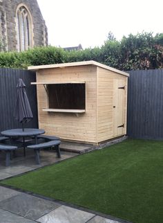 a small wooden shed sitting on top of a lush green field next to a black picnic table