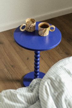 a small blue table with two cups on it and a bed in the back ground