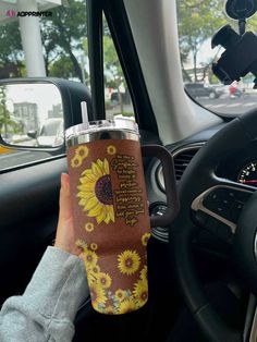 a person holding up a coffee cup in their car with the sunflowers on it