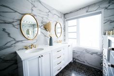 a bathroom with marble walls and two mirrors on the wall above the sinks, along with gold accents