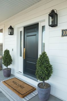 two potted plants on the front porch of a house with welcome mat and doormat