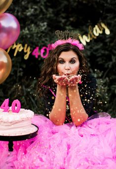 a woman sitting at a table with a cake in front of her and balloons around her