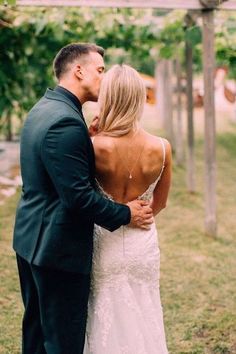 a man and woman standing next to each other in front of a wooden structure with vines on it