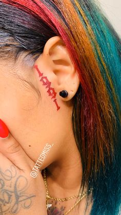 a woman with colorful hair and piercings has her hand on her face behind her ear