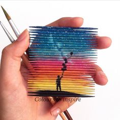 a person holding up a small piece of art made out of pencils