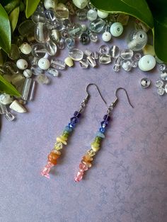 two pairs of earrings sitting on top of a table next to some beads and leaves