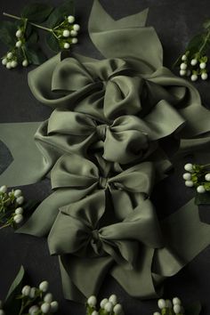 some white flowers and green leaves on a black tablecloth with grey ribbon tied around it