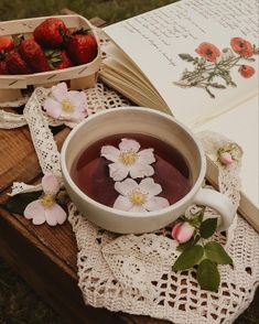 a cup of tea and some strawberries are on a table next to an open book