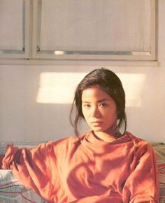 a young woman sitting on top of a bed in an orange shirt and black pants