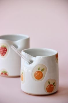 two white cups with oranges and strawberries on them, one has a spoon in it