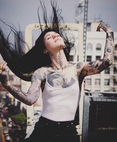 a woman with her hair blowing in the wind and tattoos on her chest, standing next to a chair