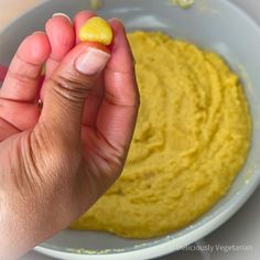 a person holding a piece of food in front of a bowl with yellow substance on it