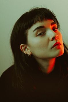 a woman with dark hair and piercings looking off to the side in red light