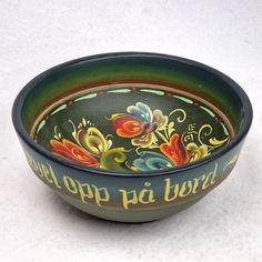 a colorful bowl with words painted on it sitting on a white counter top next to a spoon