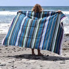 a person standing on the beach with a towel wrapped around their shoulders and holding it up