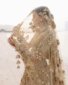 a woman in a wedding dress standing on the beach with her veil draped over her head