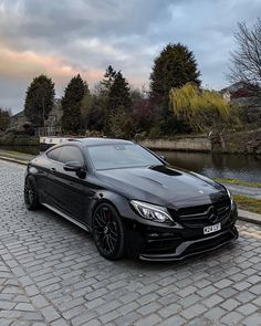 a black car parked on the side of a road next to a body of water