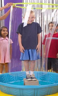 a group of children standing in front of a plastic water fountain with a girl smiling at the camera