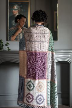 a woman standing in front of a mirror wearing a crocheted shawl with an intricate design