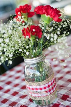 red carnations and baby's breath in a mason jar on a checkered tablecloth