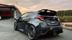 the rear end of a black sports car parked in front of a building with its trunk open