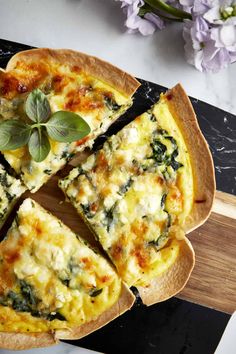 a pizza sitting on top of a wooden cutting board next to purple flowers and a knife