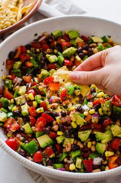 a hand dipping an egg into a bowl filled with mexican vegetables and tortilla chips