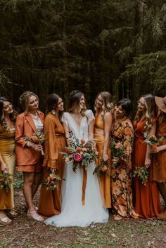 a group of women standing next to each other in front of some pine trees and bushes