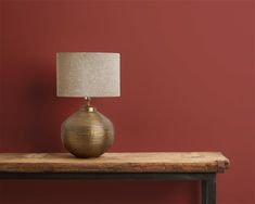 a lamp sitting on top of a wooden table next to a red wall with a black frame