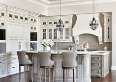 a large kitchen with white cabinets and wooden floors, an island in the middle is surrounded by gray bar stools