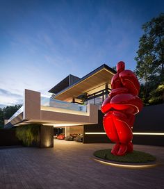 a large red sculpture in front of a modern house at night with the lights on