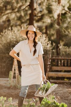 a woman wearing a hat and holding a wheelbarrow full of vegetables in the garden