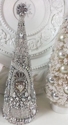 three white christmas trees with silver ornaments and pearls on the top one has an elephant figurine next to it