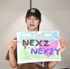 a person holding up a sign that says nexz next to her is wearing a baseball cap