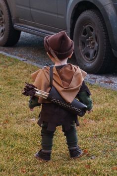 a little boy dressed up in costume standing on the grass with a book under his arm