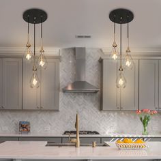 three lights hanging over a kitchen island with marble counter tops and gold faucets