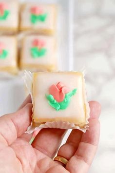 a hand holding a small square cookie with icing on it and flowers in the middle