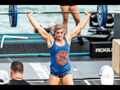 a woman lifting a barbell over her head in the middle of a crossfit competition