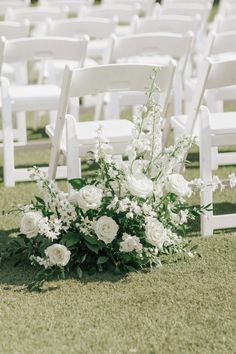 white chairs are set up in the grass for an outdoor ceremony with flowers and greenery