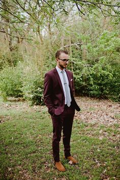 a man in a suit and tie standing in the grass with trees in the background