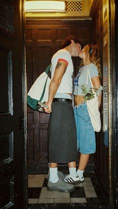 two people standing in an elevator kissing each other and one person is holding a bag