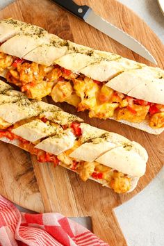 two sub sandwiches cut in half on a cutting board with a knife next to it