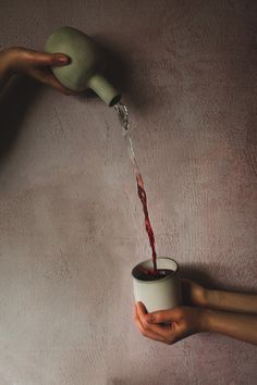 two hands are holding a cup with red liquid coming out of it, while another hand is pouring water into the cup