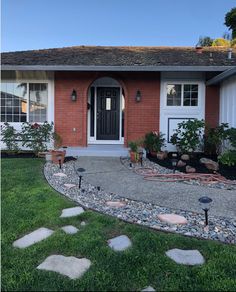 a house that has some plants in the front yard and rocks on the ground around it