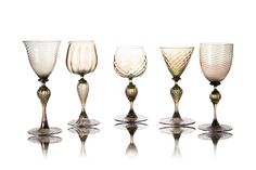 five wine goblets are lined up on a white surface, one is empty