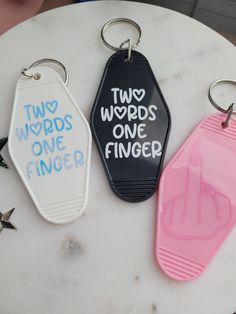 three words one finger and two fingers keychains sitting on a white marble table