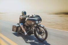 a man riding on the back of a motorcycle down a road next to a desert